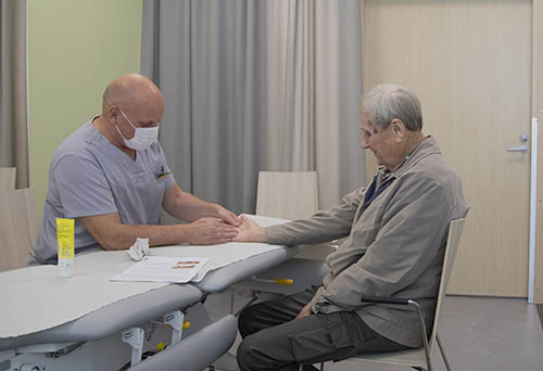 Hoitaja hoitaa vanhan herrasmiehen käsiä hoitohuoneessa.