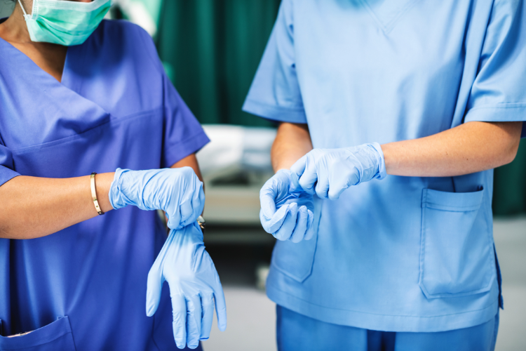 Kaksi hoitajaa pukee sinisiä kumihanskoja käsiinsä.