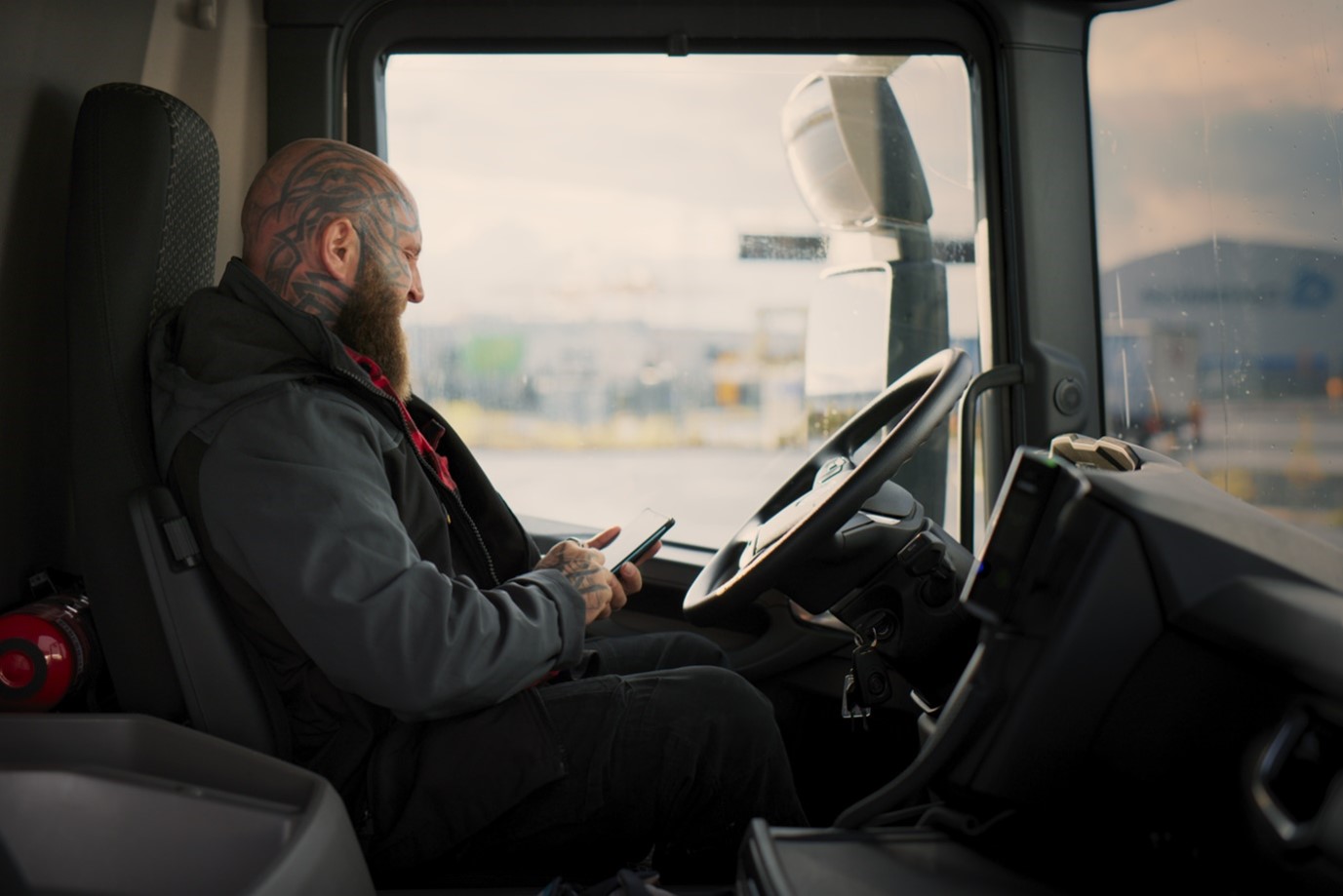 Mies istuu rekka-auton ratissa puhelinta kädessään pidellen.