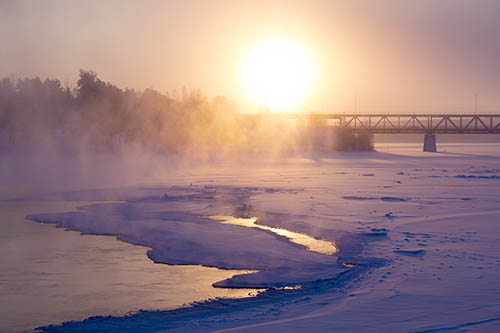 Silta yli jäätyneen joen talviauringossa.