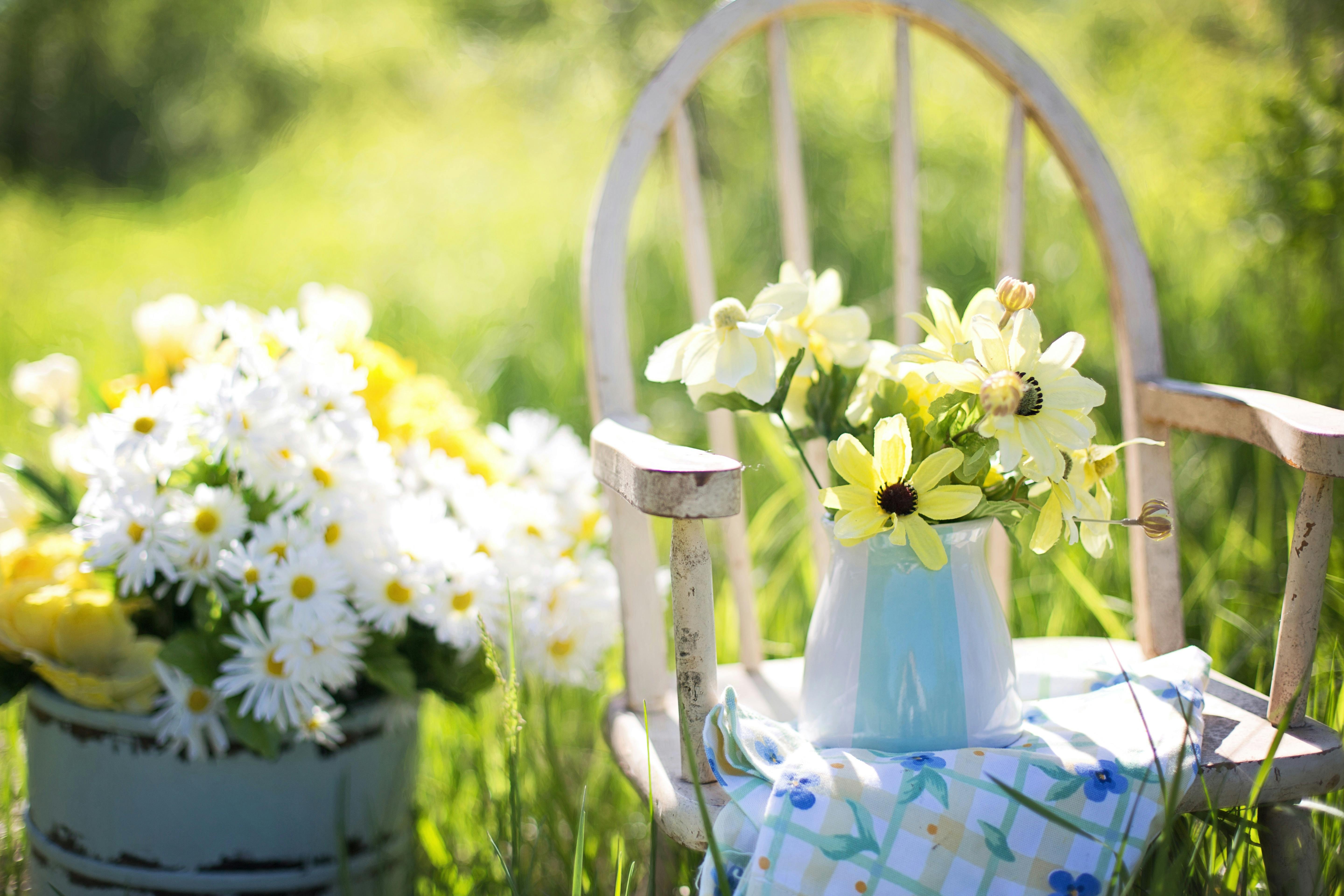Kesäinen ulkokuva, jossa kukkia maljakossa pöydällä ja tuolilla.